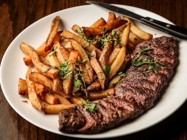 Sliced flat iron steak served with hand-cut fries and fresh herbs